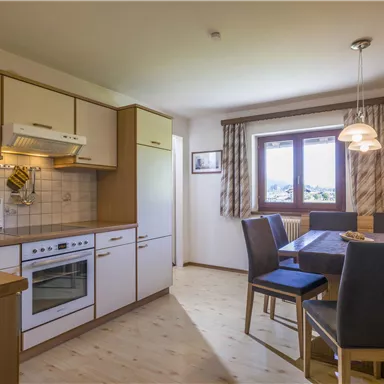 A modern kitchen with wooden cabinets and a dining table. Next to the window, there are chairs and a warm, inviting space.