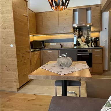 A modern kitchen made of wood with a dining table and elegant lighting. The furnishings are functional and cozy.