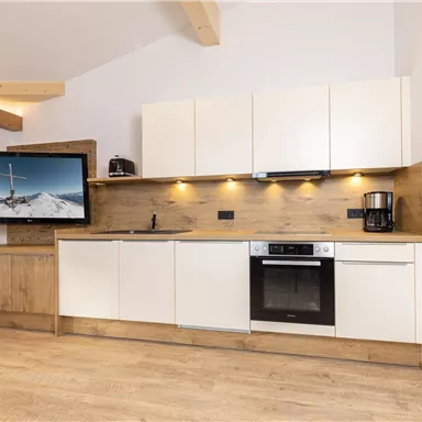 A modern kitchen with bright cabinets and wooden accents. A TV hangs on the wall, and the furnishings are functional and stylish.
