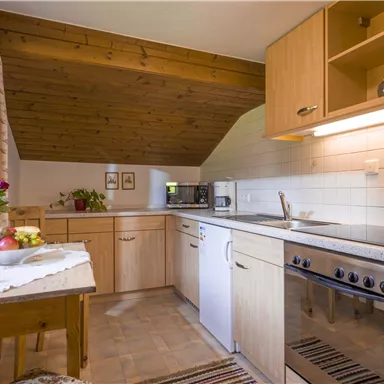 A bright kitchen with wooden shelves and modern appliances. Flowers and fruit are on the table.