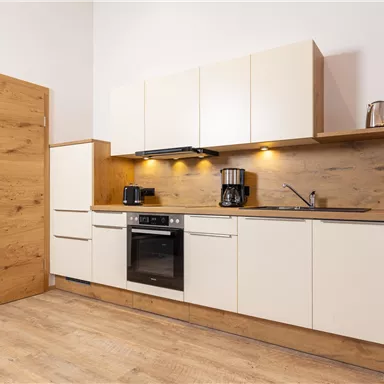 A modern kitchen with bright cabinets and a wooden countertop. In the background, kitchen appliances and a window can be seen.