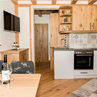 Eine moderne Küche mit Holzschränken und einem eleganten Design. Im Vordergrund steht ein Tisch mit einer Flasche Wein und frischen Blumen.