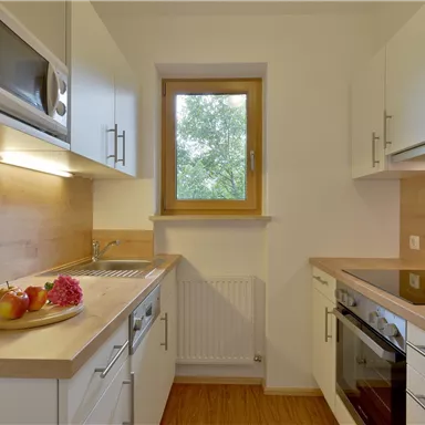 A modern kitchen with white cabinets and hardwood surfaces. A window lets in natural light, there is fruit on the countertop.