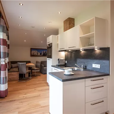 A modern kitchen with a bright design and wooden flooring. In the background, an inviting living area is visible.