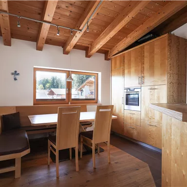 Modern kitchen with wooden beam ceiling and large windows. The room features a dining area with elegant wooden furniture and a cozy atmosphere.