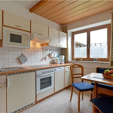A modern kitchen with bright furniture and a wooden ceiling. The table is set with a fruit bowl and a window provides daylight.