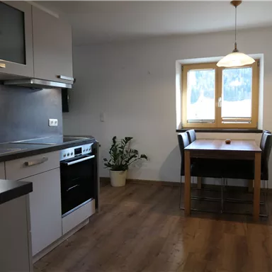 A modern kitchen with a dining table and four chairs. The walls are light and a window provides natural light.