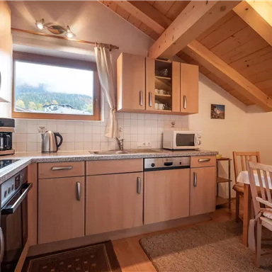 Eine gemütliche Küche mit Holzschränken und modernen Geräten. Ein Esstisch mit Stühlen befindet sich in der Ecke und bietet einen Blick auf die Landschaft durch das Fenster.