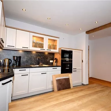 A modern kitchen with white cabinets and a dark countertop. The dining area is furnished with a wooden table and several chairs.