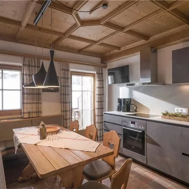 Eine moderne Küche mit Holzdecke und gemütlicher Sitzecke. Der Tisch ist mit dekorativen Elementen gedeckt und es gibt große Fenster, die viel Licht hereinlassen.