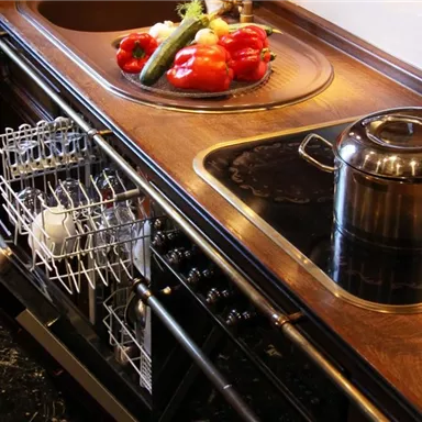 A modern kitchen with a dishwasher and a pot on the stove. Fresh vegetables are on the kitchen table.
