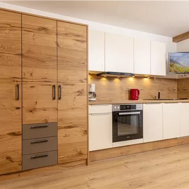 A modern kitchen with wooden cabinets and white fronts. It is well equipped with a stove, a refrigerator, and a television.