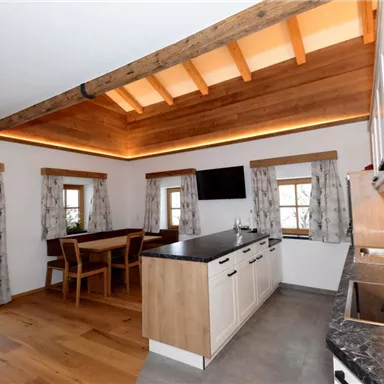 A modern kitchen with wooden shelves and large windows. The room is bright and inviting, with a dining table and a comfortable atmosphere.