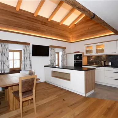 A modern kitchen with wooden cladding and a cozy dining area. Bright colors and large windows create an inviting atmosphere.