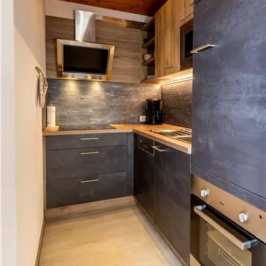 Eine moderne Küche mit Holzdecke und eleganten, dunklen Schränken. Die Ausstattung umfasst einen Herd, einen Kühlschrank und eine Mikrowelle.