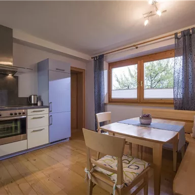 Eine moderne Küche mit Holzfußboden und hellen Wänden. Daneben ein Essbereich mit einem Tisch und Stühlen.