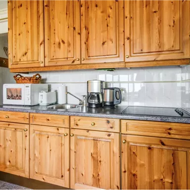 Eine gemütliche Küche mit Holzschränken und einer modernen Ausstattung. Im Hintergrund sind ein Wasserkocher und eine Kaffeemaschine sichtbar.
