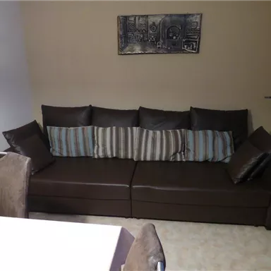 A modern living room with a stylish brown sofa and decorative cushions. In the background, light walls and a picture can be seen.