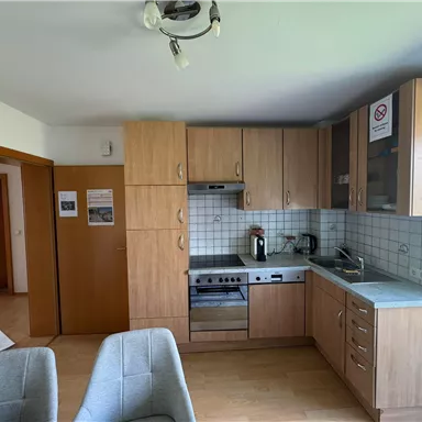 A modern kitchen with wooden cabinets and a stove. There is a coffee machine by the window and the walls are tiled in light colors.