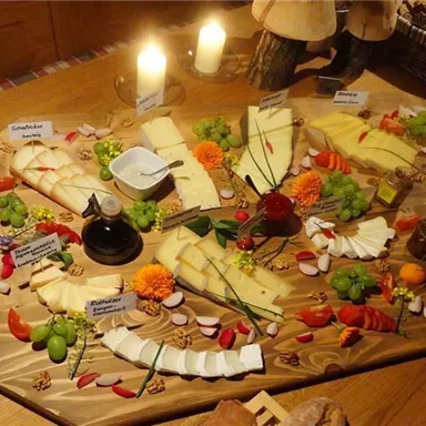A rich cheese buffet with various types of cheese, grapes, and fresh vegetables. The presentation is appealingly arranged on a large wooden board.
