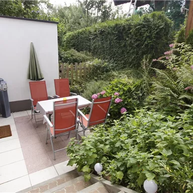 Ein einladender Gartenbereich mit einem Tisch und Stühlen. Umgeben von üppigem Grün und bunten Blumen schafft er eine entspannte Atmosphäre.