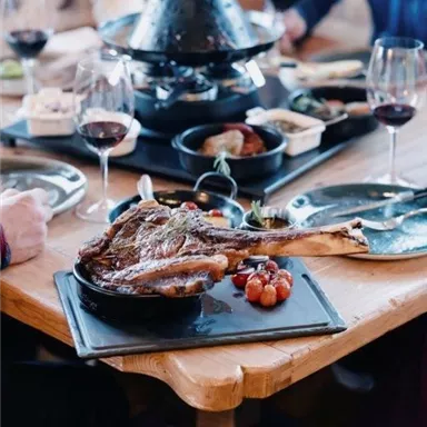 A hearty dinner with meat, vegetables, and several side dishes on a table. Red wine and glassware enhance the festive atmosphere.