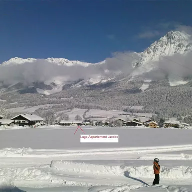 A snowy landscape with mountains in the background. In the foreground, a child stands in a snow-covered field.