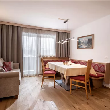 A cozy living space with a table and chairs. Daylight streams in through a large window.