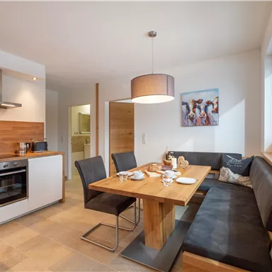 A modern kitchen with a dining table and a cozy bench. The walls are light, and there is a pendant lamp above the table.