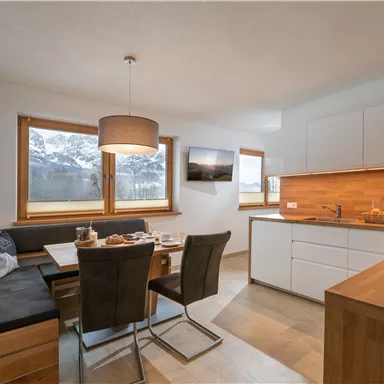A modern kitchen with a dining area and large windows that offer a view of the mountains. The space is bright and cheerfully furnished.