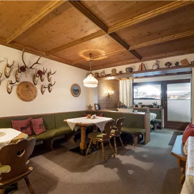 Ein gemütliches Restaurant mit Holzmöbeln und einer rustikalen Innenausstattung. An der Wand hängen Geweihen und die Tische sind für Gäste gedeckt.