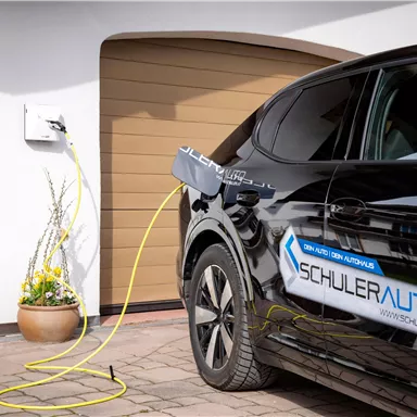 Ein schwarzes Elektroauto wird an einer Ladestation aufgeladen. Im Hintergrund ist eine Garage zu sehen.