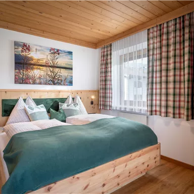 Ein gemütliches Schlafzimmer mit einem Doppelbett und Holzverkleidung. Das Zimmer hat ein Fenster mit Vorhängen und ein Bild an der Wand.