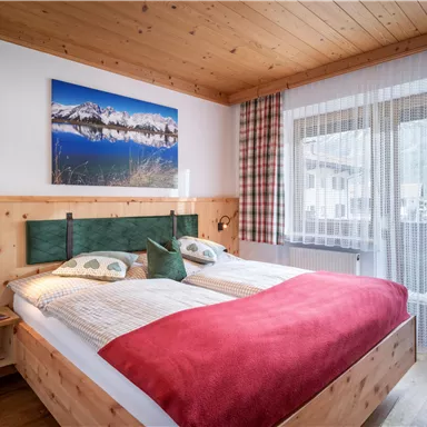 Ein gemütliches Schlafzimmer mit einem großen Bett und Holzdekor. Der Raum hat einen Balkon und ein schönes Bild von Bergen an der Wand.