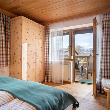 Ein gemütliches Schlafzimmer mit Holzdecke und karierten Vorhängen. Der Balkon bietet einen Blick auf die Umgebung und frische Luft.