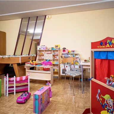 Ein bunter Spielbereich mit verschiedenen Spielzeugen, darunter ein Puppentheater und ein Billardtisch. Die Wände sind hell und der Raum wirkt einladend für Kinder.