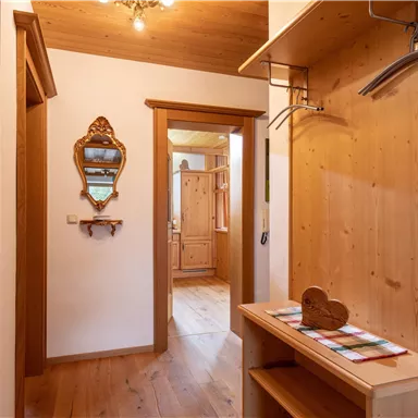 Ein gemütlicher Eingangsbereich mit Holzwänden und einem Spiegel. Der Boden ist aus Holz, und ein kleiner Tisch steht neben einer Garderobe.