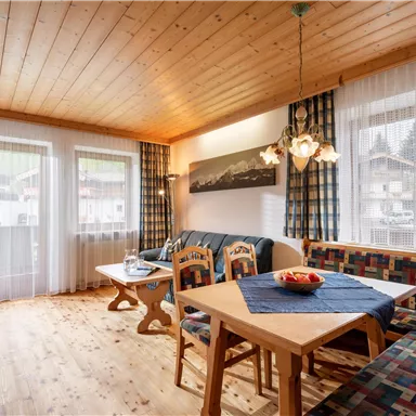 Ein gemütlicher Wohnbereich mit Holzboden und großen Fenstern. Eine Sitzgruppe sowie ein Tisch laden zum Entspannen und Verweilen ein.