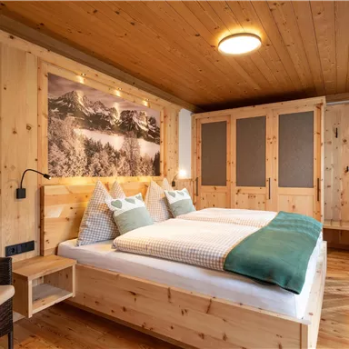 Ein gemütliches Zimmer mit Holzverkleidung und einem Doppelbett. Der Raum ist hell und freundlich, mit einem schönen Blick auf Berge.