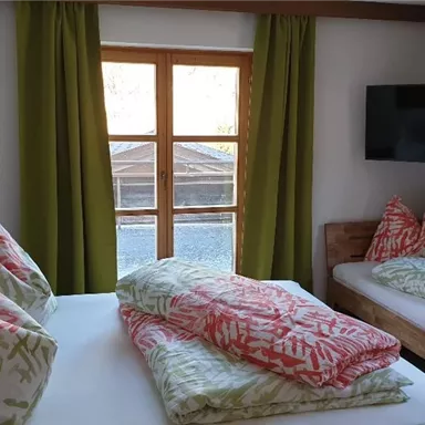 A cozy room with two beds and colorful cushions.  
Large windows let in plenty of light and offer a view outside.