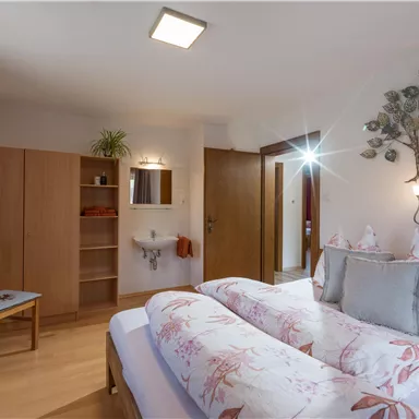 A cozy bedroom with a large bed and floral decorative pillows. There are wooden furniture and a small vanity in the room.