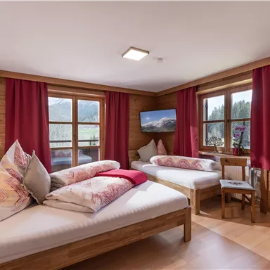 A cozy bedroom with two single beds and colorful cushions. Large windows provide a view of nature and allow plenty of daylight.