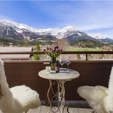 A balcony with a view of snow-capped mountains. Two comfortable chairs and a small table with flowers and glasses invite you to linger.