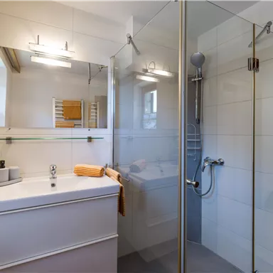 A modern bathroom with a shower and a sink. The walls are light and the room is well-lit.
