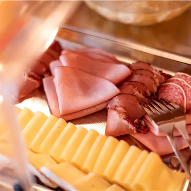 Ein Buffet mit verschiedenen Wurst- und Käsesorten. Mehrere Scheiben Schinken und Käse sind auf einem Tablett angeordnet.