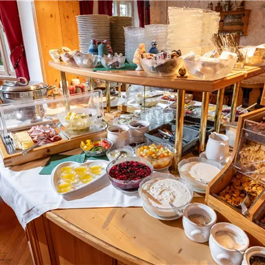 Ein reichhaltiges Frühstücksbuffet mit frischem Obst, Joghurt, verschiedenen Aufschnittsorten und verschiedenen Snacks. Der Tisch ist einladend und gut dekoriert.