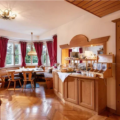 Ein einladender Frühstücksraum mit Holzmöbeln und großen Fenstern. Auf dem Tisch sind Snacks und Getränke bereitgestellt.