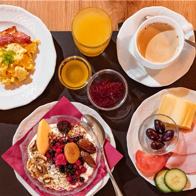 Ein reichhaltiges Frühstück mit Rührei, Speck, Müsli und frischen Früchten. Dazu gibt es verschiedene Getränke, einschließlich Kaffee und Saft.