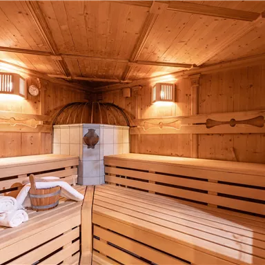 Eine gemütliche Sauna mit Holzbänken und sanfter Beleuchtung. Im Raum befinden sich eine Holzkelle und mehrere Handtücher.