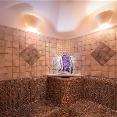 Ein eleganter Spa-Raum mit mosaikverkleidetem Sitzbereich und einer dekorativen Wand mit einem amethystfarbenen Mineral. Sanftes Licht sorgt für eine entspannende Atmosphäre.
